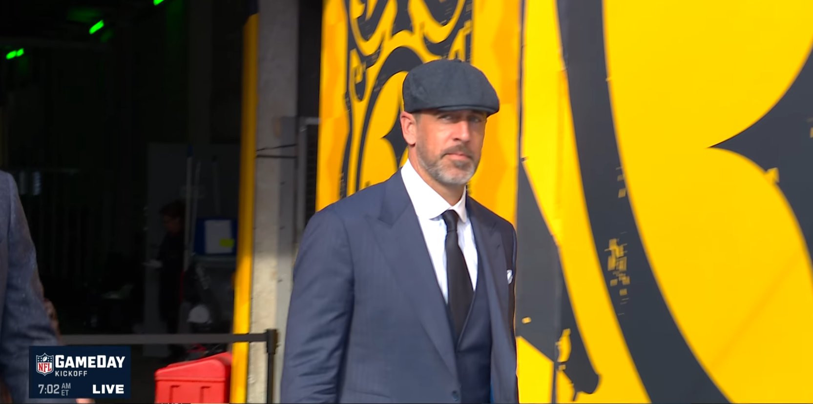 Aaron Rodgers wearing a navy suit and flat cap before the Steelers–Saints game